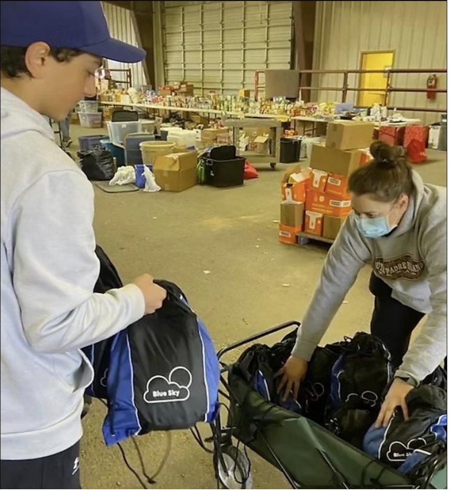 Two volunteers organizing rows of Blue Sky relief kits for distribution