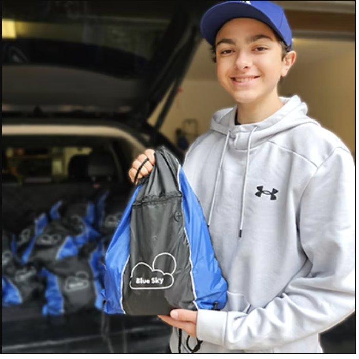 A young volunteer holding a Blue Sky relief kit, with a carload of kits ready for delivery